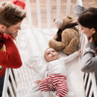 High view of mom and dad peering in crib at baby