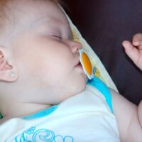 Baby girl asleep in stroller with orange pacifier