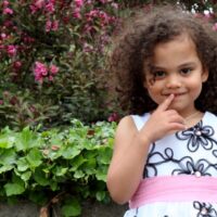 Curly, dark haired preschooler in front of flower bushes