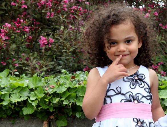Curly, dark haired preschooler in front of flower bushes