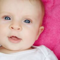 Blue eyed baby girl laying on pink blanket