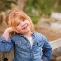 Little girl with red hair posing at the park against a fence