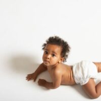 Curly haired baby boy in diaper crawling on white floor