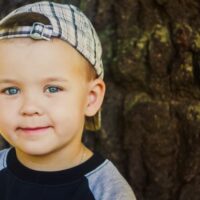 Blue eyed young boy with plaid hat on backwards