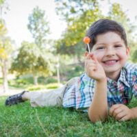 Dark haired boy laying outside enjoying his lollipop