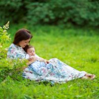 Baby and mama sitting outdoors in grass by flowering bush