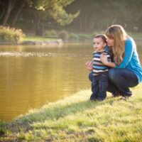 Mom and toddler boy looking together at water outdoors