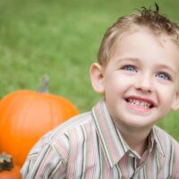 Smiling school aged boy sitting with pumpkins