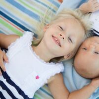 Happy big sister laying with baby brother on blanket