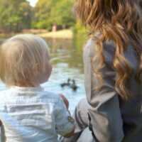 Mom with toddler outdoors feeding the ducks in lake