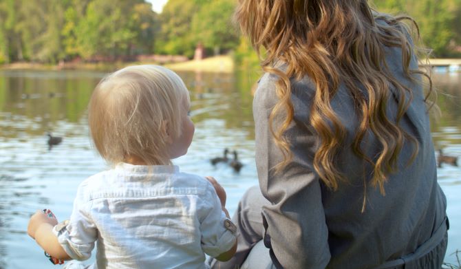 Mom with toddler outdoors feeding the ducks in lake