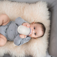 Baby drinking bottle on cream blanket in gray outfit