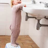 toddler on step stool in front of sink