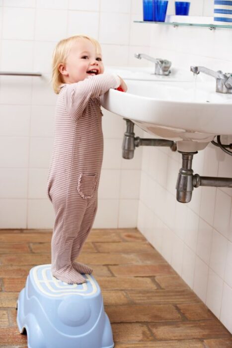 toddler on step stool in front of sink