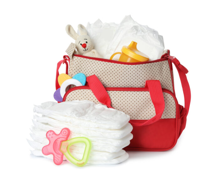 Large diaper bag with disposable diapers and baby toys on white background