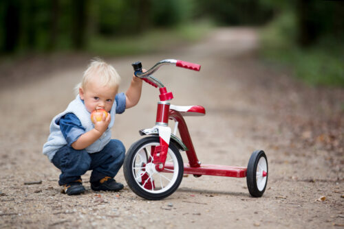 toddler boy sitting with his tricycle outside