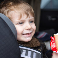 Child eating ice cream and smiling in his car seat