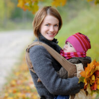 Mom with baby in carrier with fall leaves in her hand