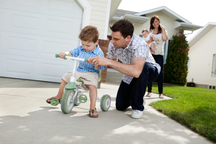 toddler riding on a tricycle outside with dad
