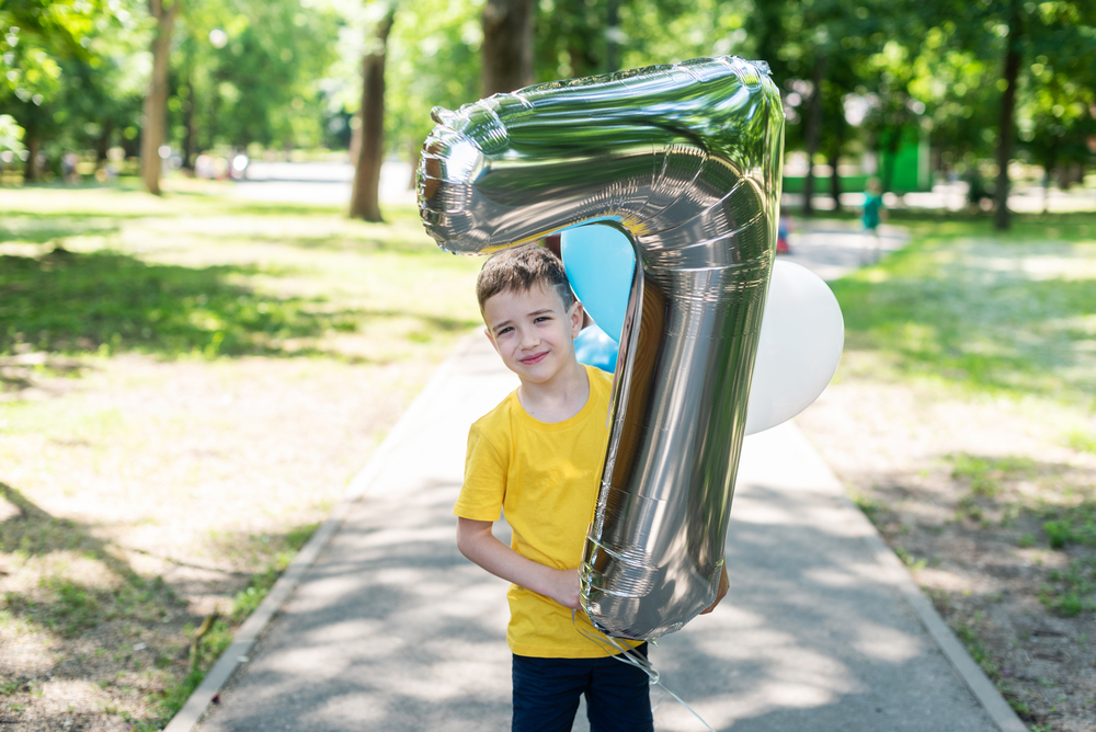 Little boy in yellow shirt with #7 balloon