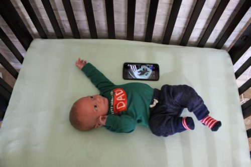 baby laying in crib with mobile phone connected to baby monitor app