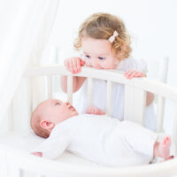 Toddler looking at baby in crib