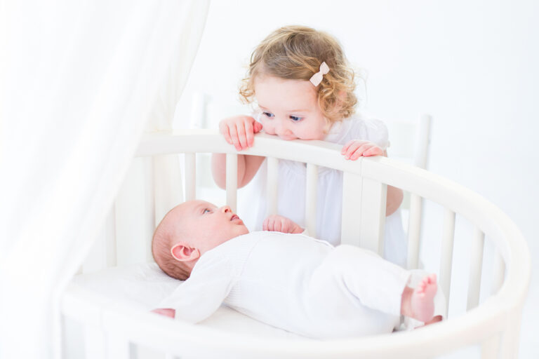 Toddler looking at baby in crib