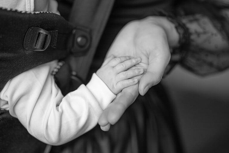 Mom and baby holding hands in baby carrier