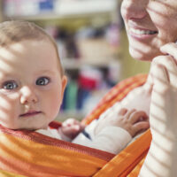 Close up of blue eyed baby with mom in sling baby carrier
