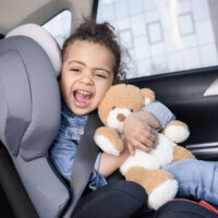 child sitting in a car seat with her teddy bear