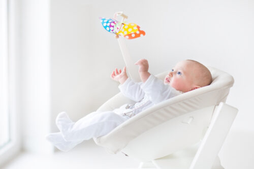 baby sitting in a rocker playing with mobile