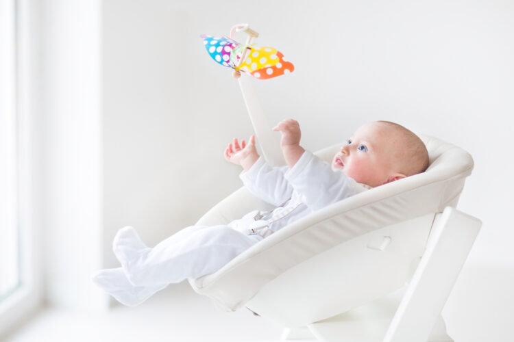 baby sitting in a rocker playing with mobile
