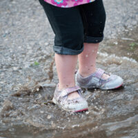 toddler standing in a puddle with water shoes on