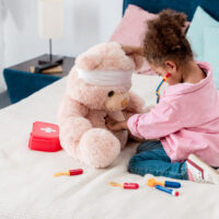 Little girl in pink playing doctor with teddy bear