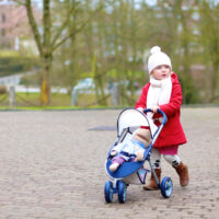 Little girl pushing baby stroller with baby doll