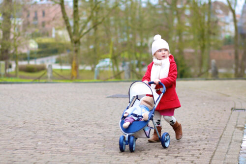 Little girl pushing baby stroller with baby doll