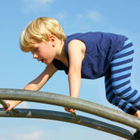 A cute little boy is carefully climbing a ladder toy at the playground on a summer day