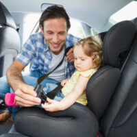 Dad strapping baby girl in car seat