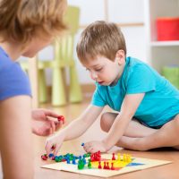 Mother and her son playing in board game on floor in nursery