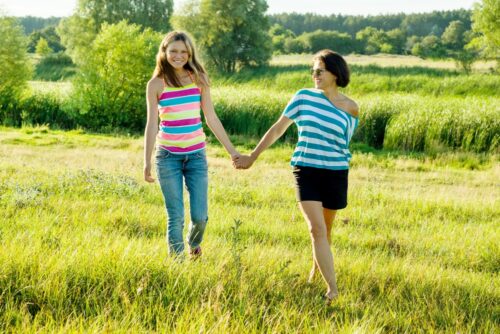 Mom walking with teen daughter in green field