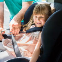 toddler getting buckled into a car seat