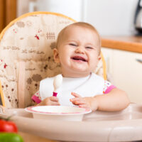 baby smiling in high chair eating food