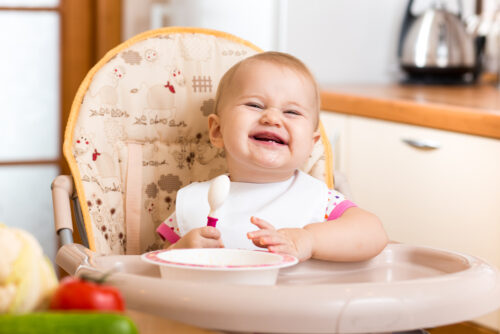 baby smiling in high chair eating food