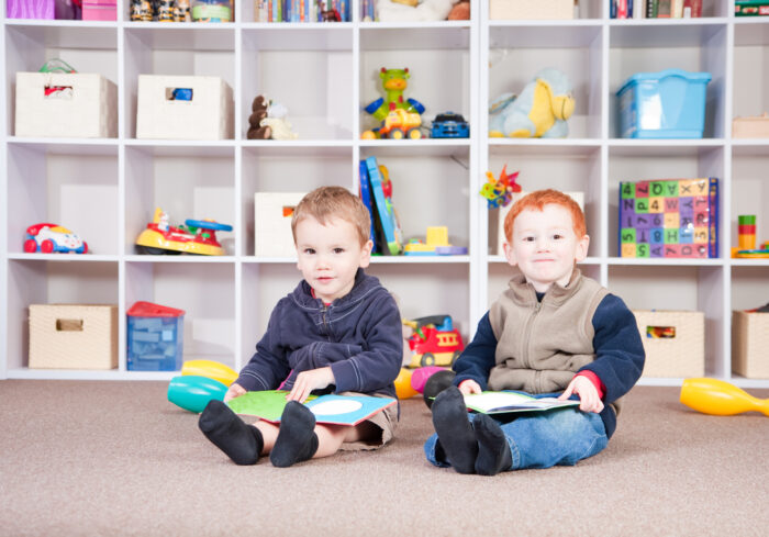 Two toddlers reading in front of toy and book shelves