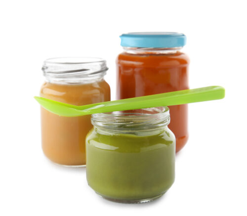 Jars with baby food and spoon on white background