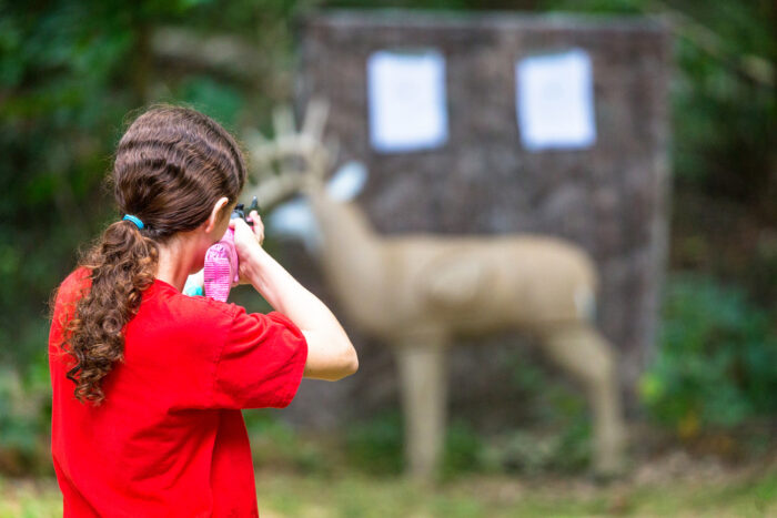 Young girl practcing target shooting with a bb gun at a model deer in the woods