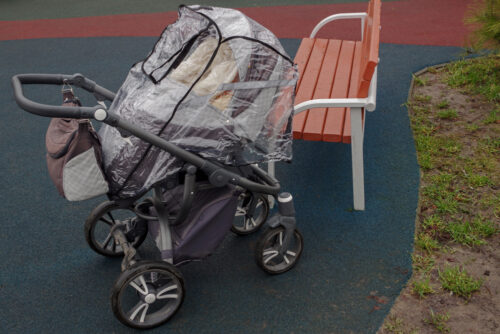 Empty stroller covered with stroller rain cover at playground on rainy day