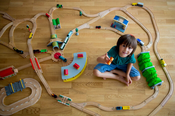young boy sitting with large wooden train set