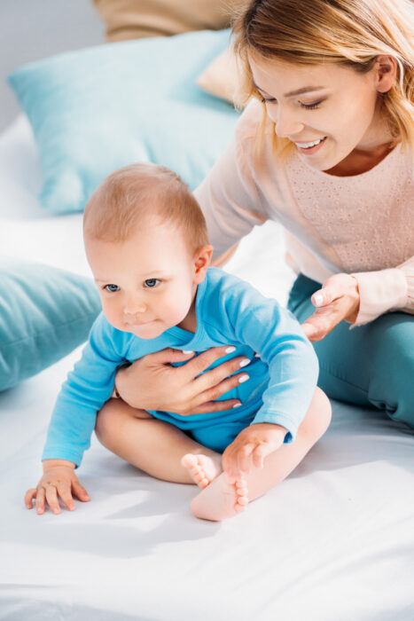 woman helping baby sit up on bed