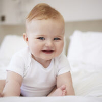 Smiling Baby Trying to Sit Up on Bed